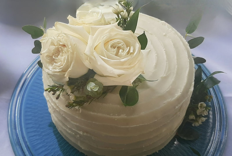 A white-iced celebration cake decorated with fresh roses and eucalyptus